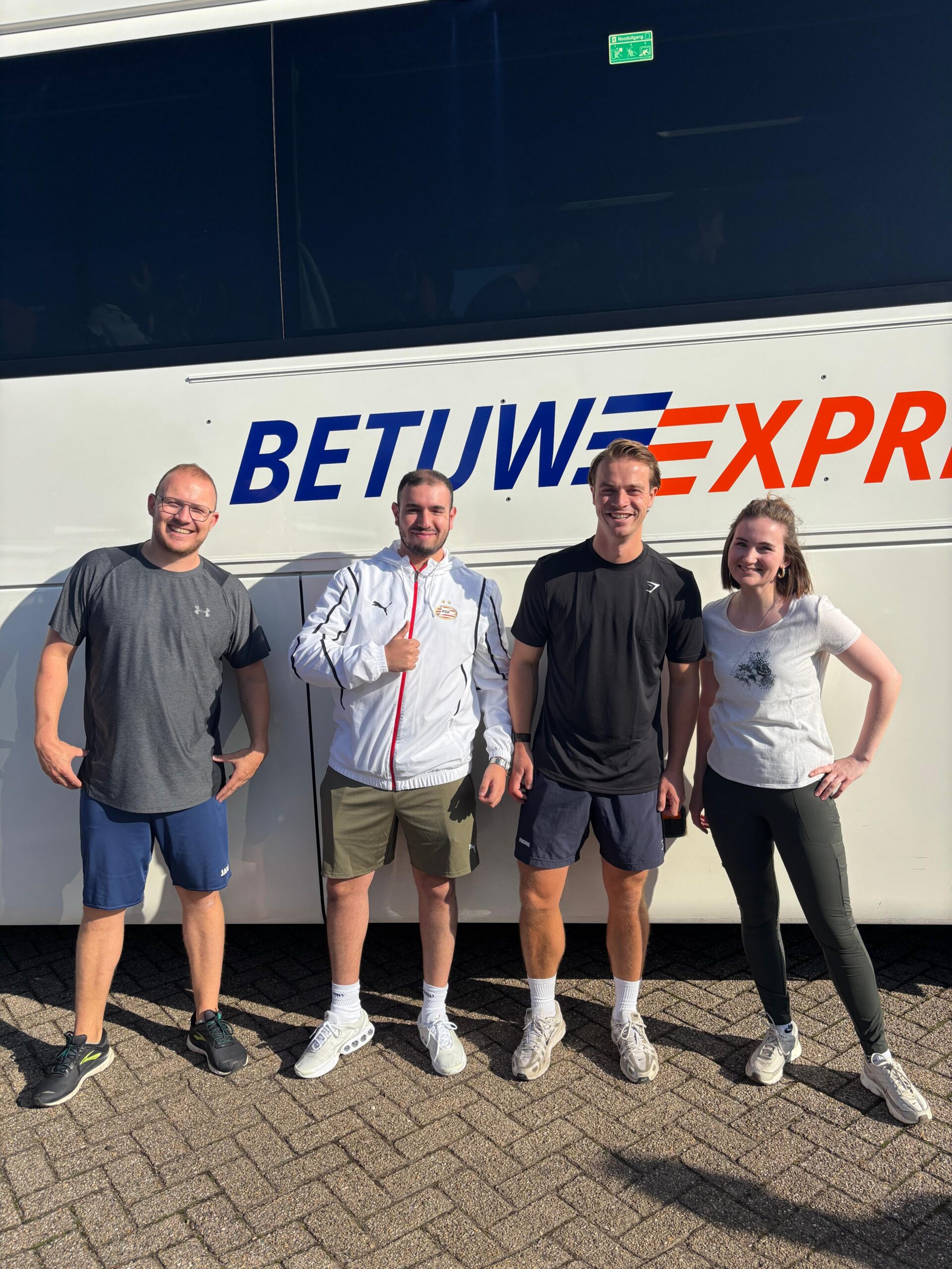 Vier jonge volwassenen lachend voor een touringcar