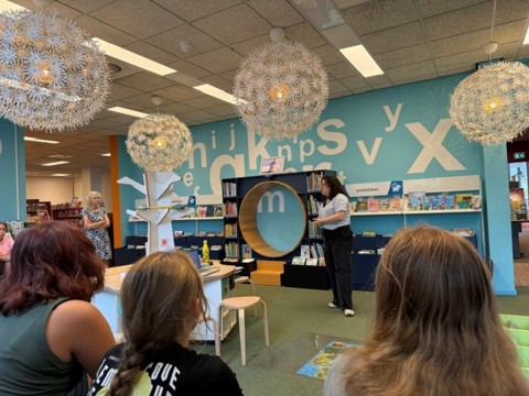 Drie kinderen zittend op kussens in de bibliotheek luisterend naar een verhaal